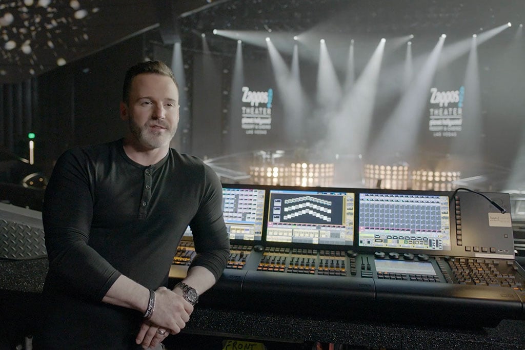 Man sitting in front of multiple monitors with a stage in the background