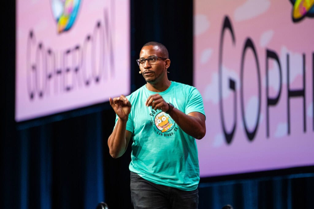 Man in a bright green T-shirt speaking on stage at a conference