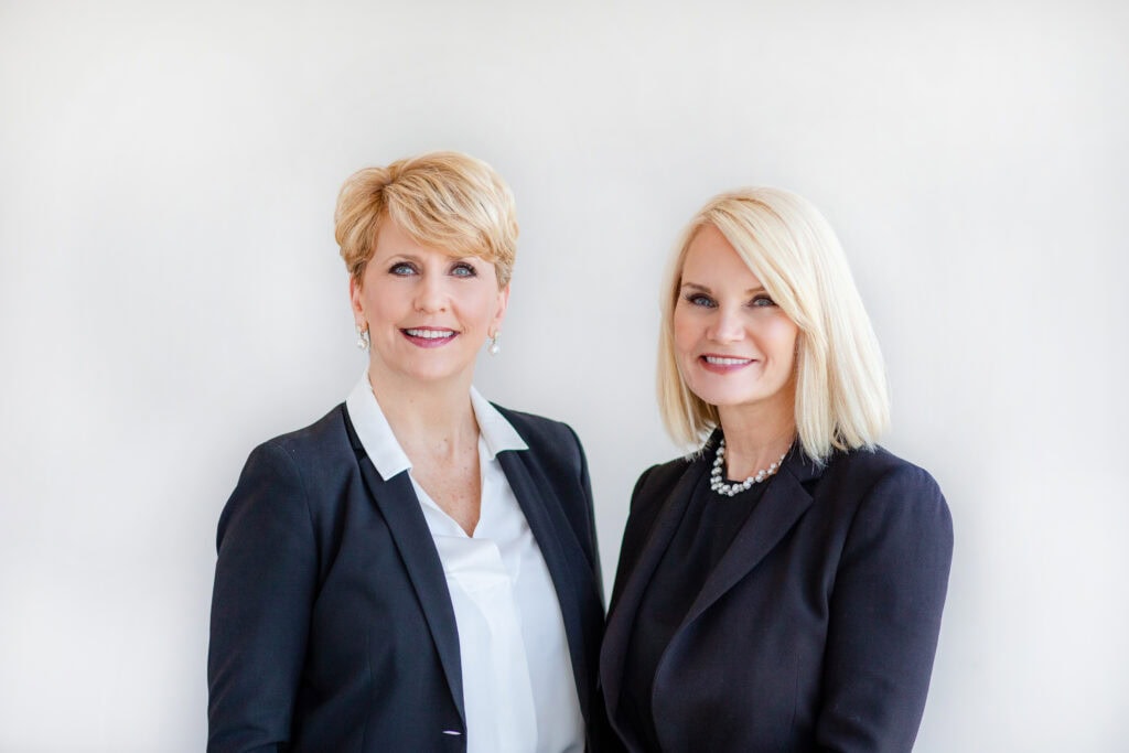 Two women in business attire pose for a portrait