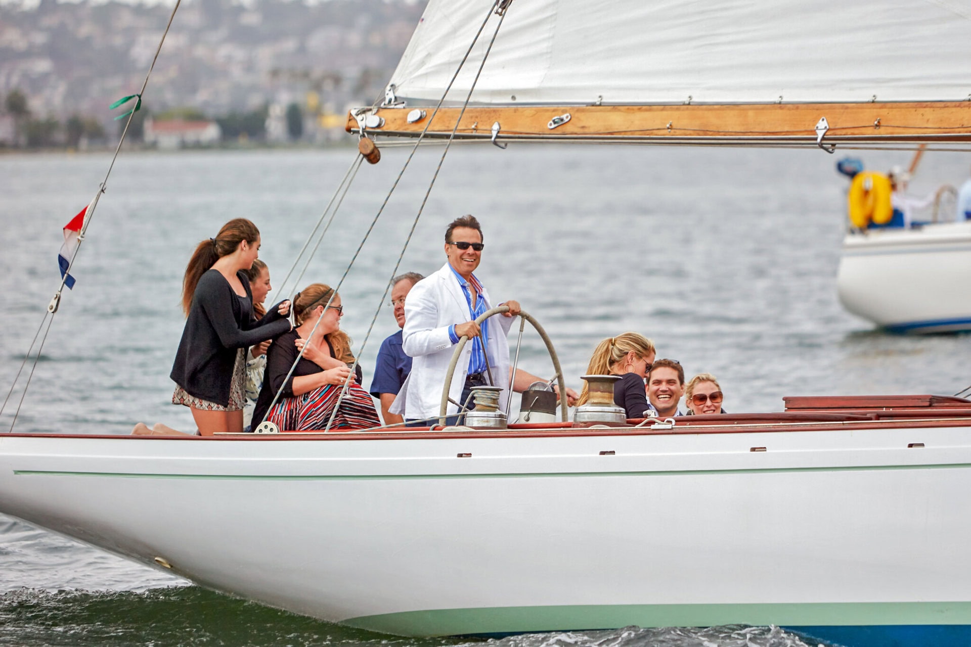 A group of people on a sailboat, with a man at the helm