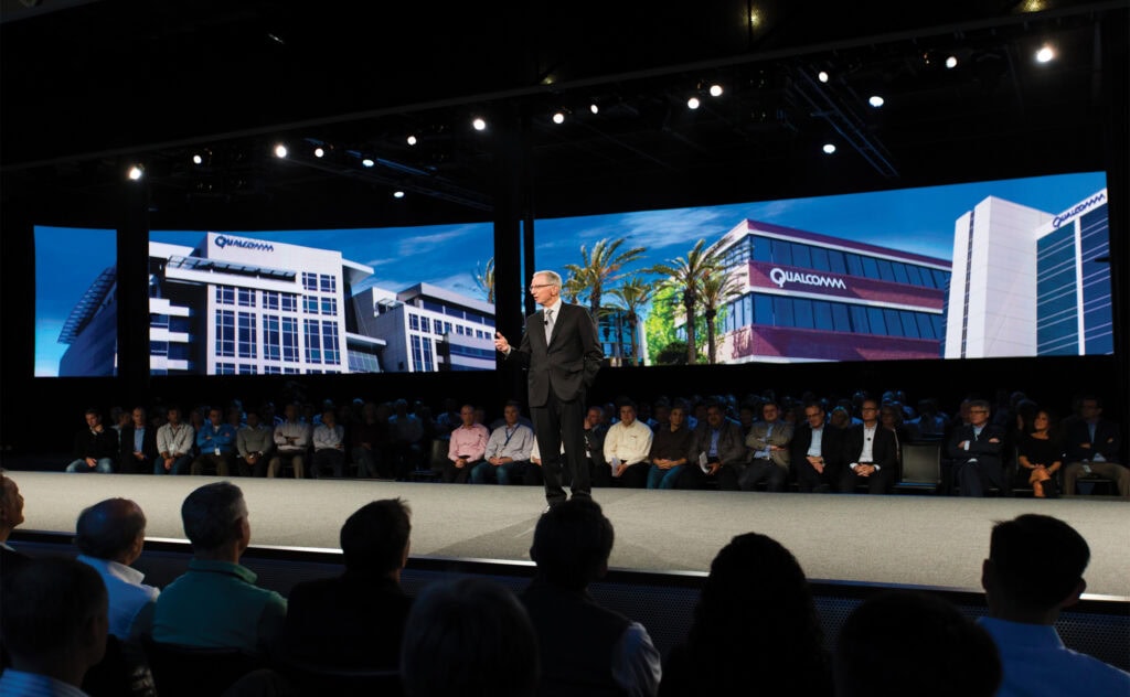 Man in a suit speaking on stage at a convention