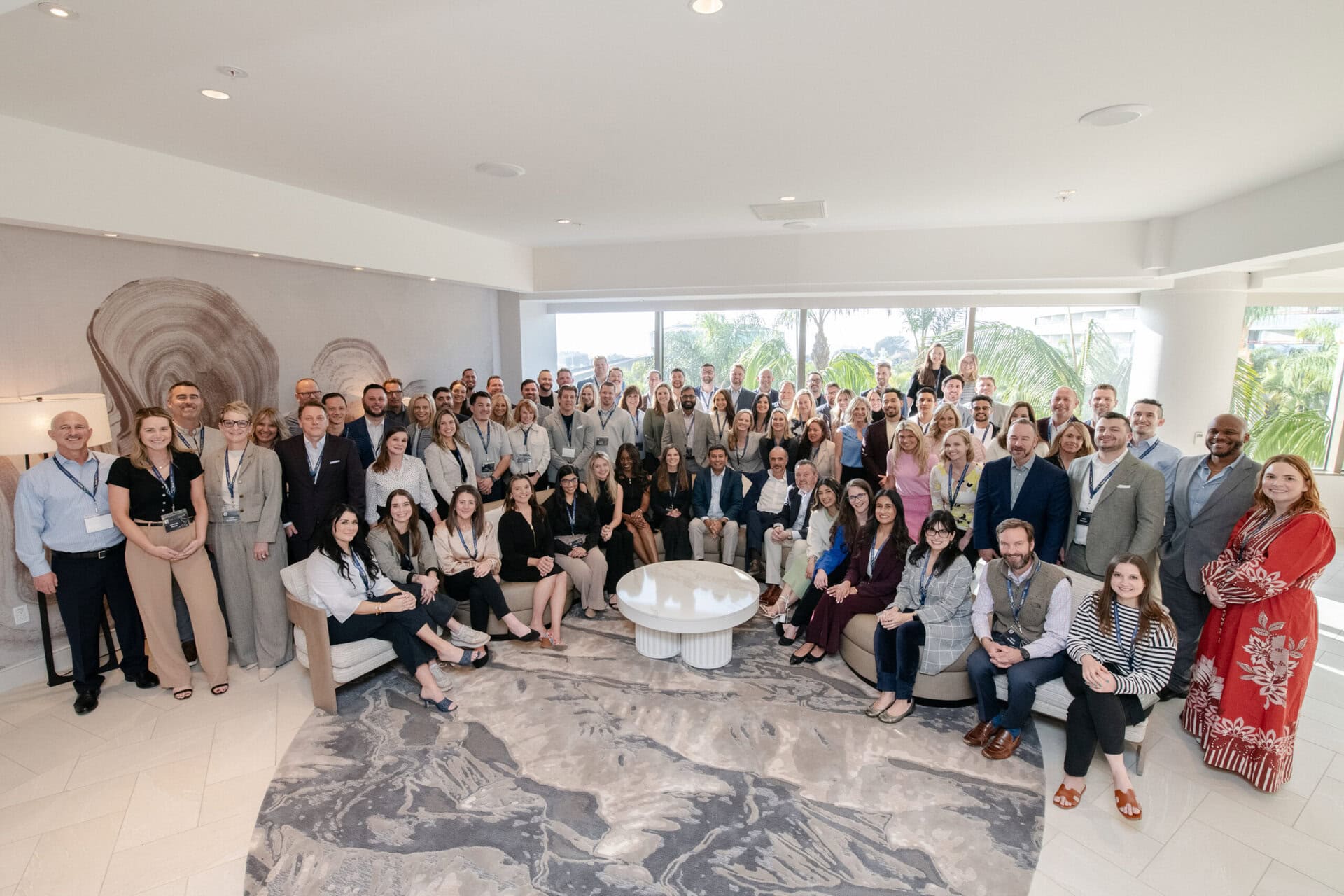 A 50+ person business staff posing for a group photo in a white room filled with natural light.