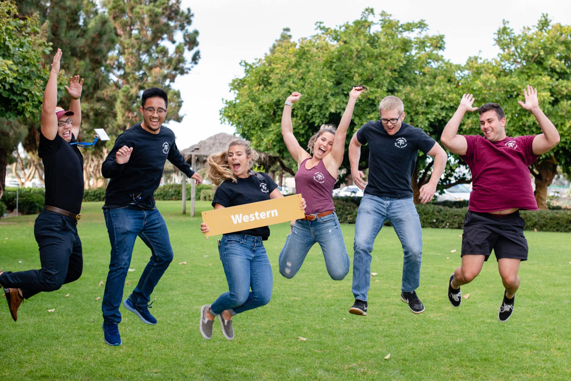 A group of people jumping into the air and holding their hands up on a grassy field