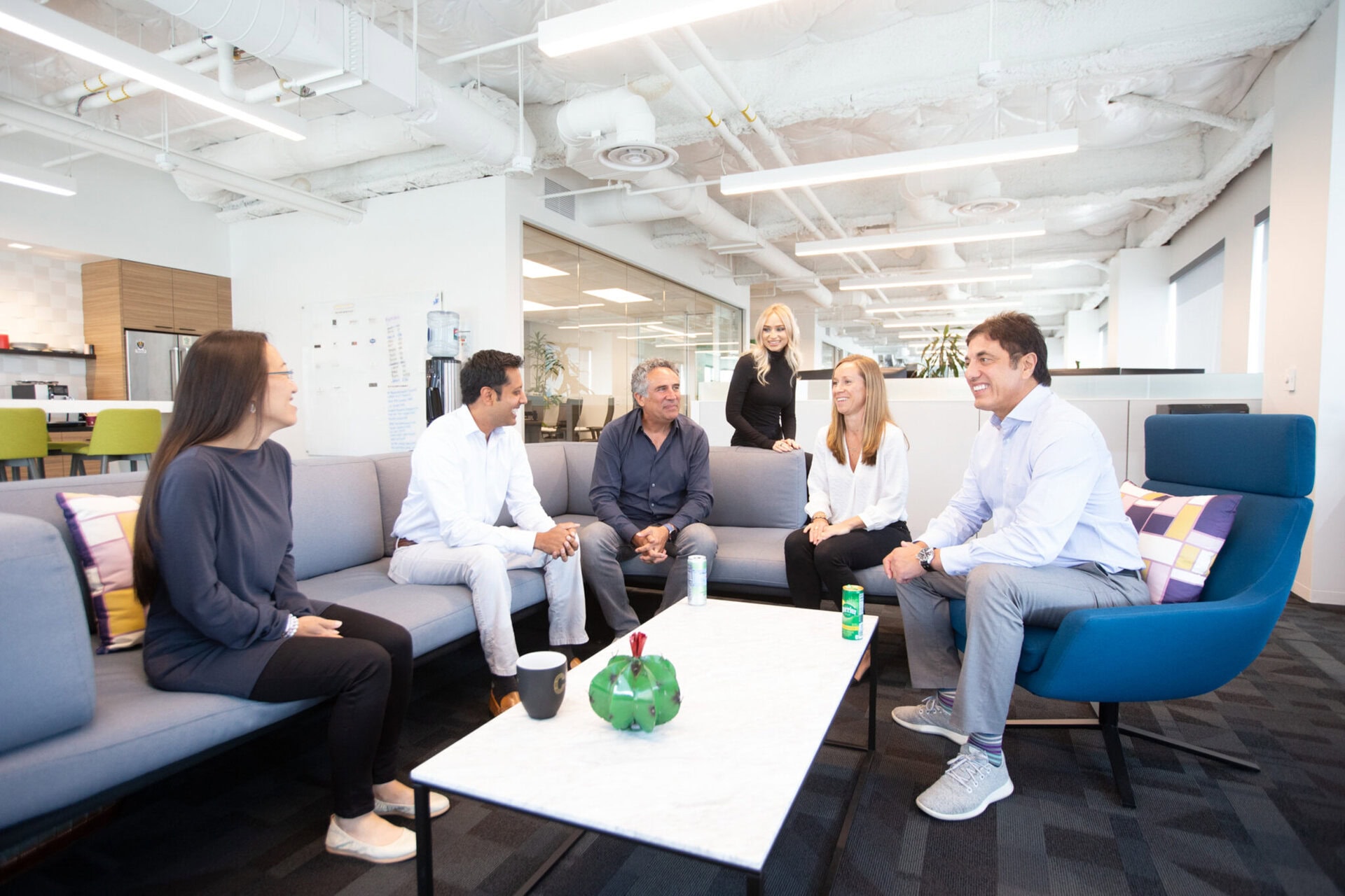 A small group gathers around chairs, couches and a coffee table in a modern office