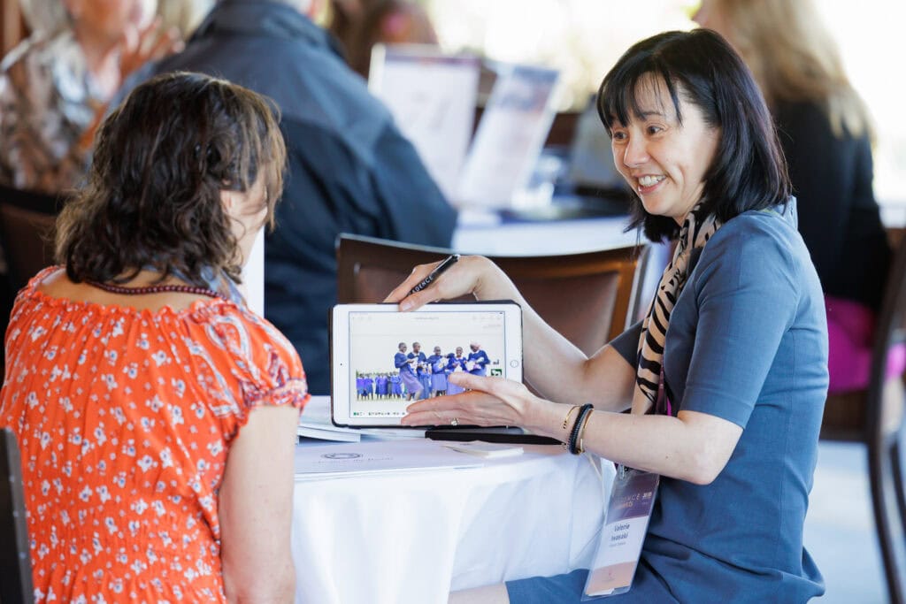 A woman showing images on a tablet to another woman during a business event