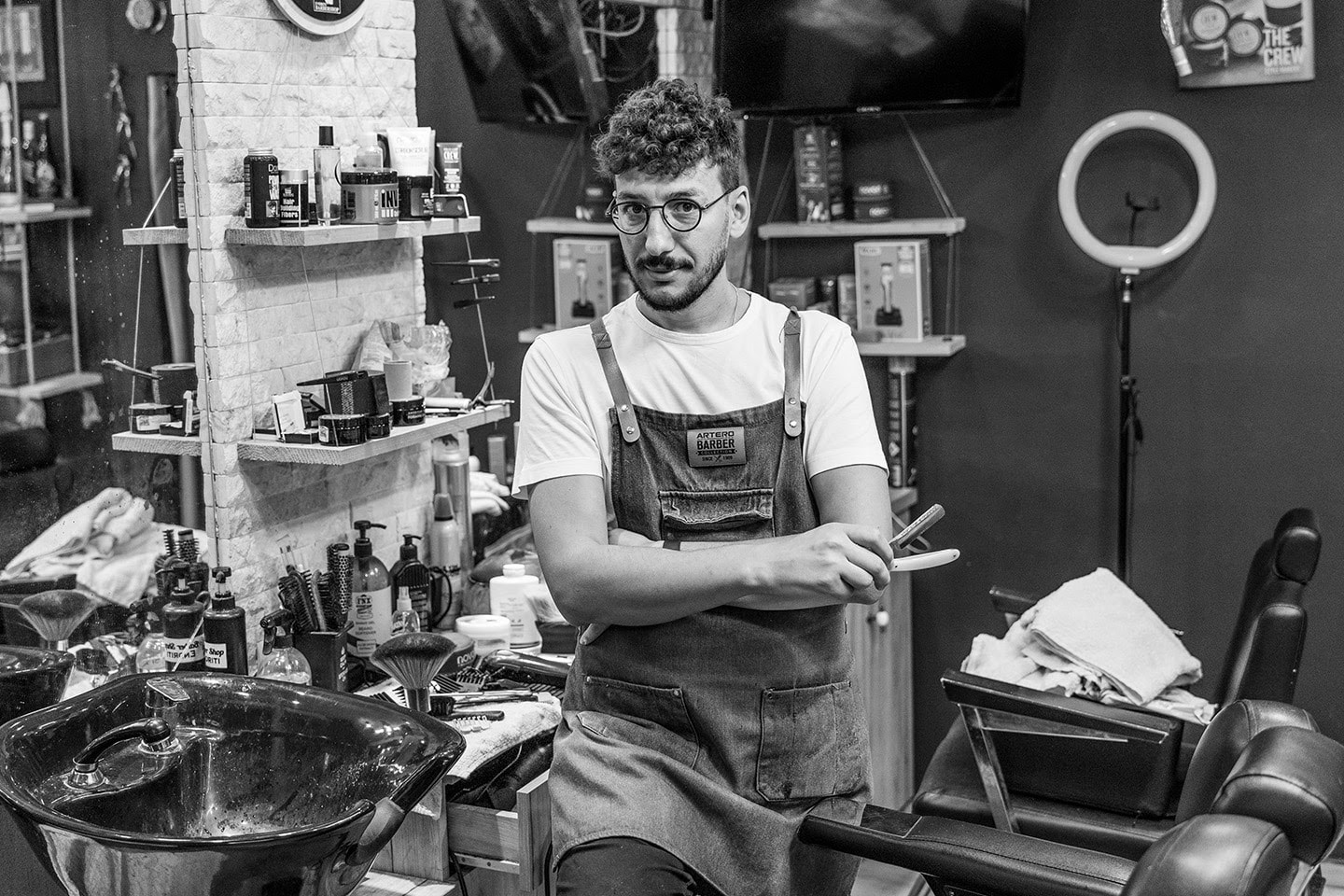 A barber in overalls and glasses in a barber shop