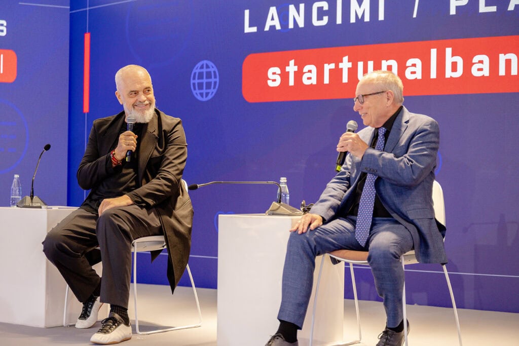 Two men in suits on stage at a conference in Albania