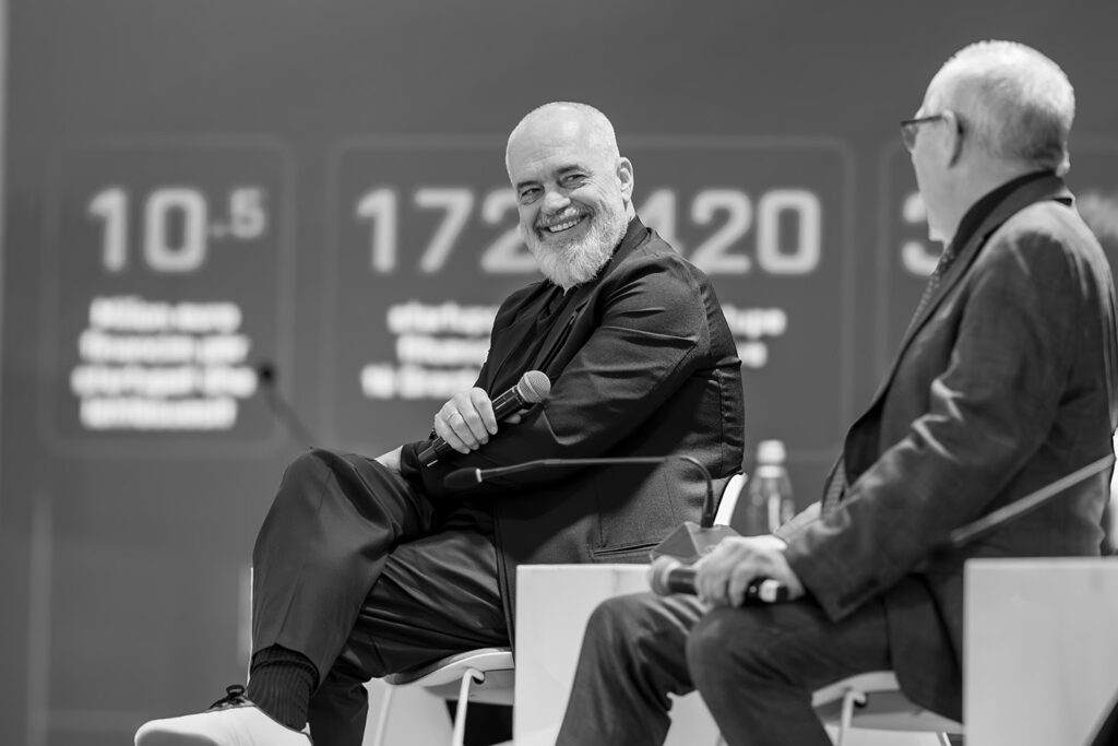 Two men in conversation, holding microphones on stage during a conference.