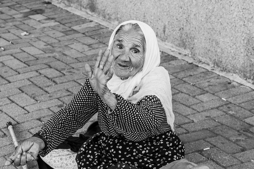 An elderly woman in a headscarf sitting on the street in Albania