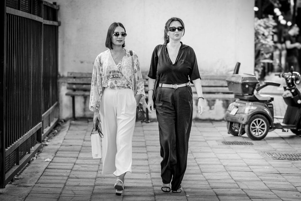 Two women walk down a street in Albania, holding bags and purses