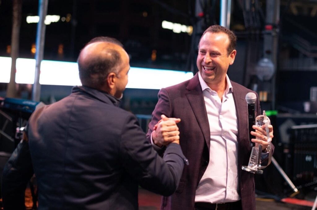 Two men smile and shake hands on stage during a business conference.