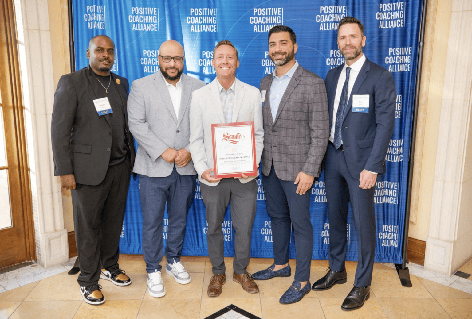 five men in suits stand together holding up an award.