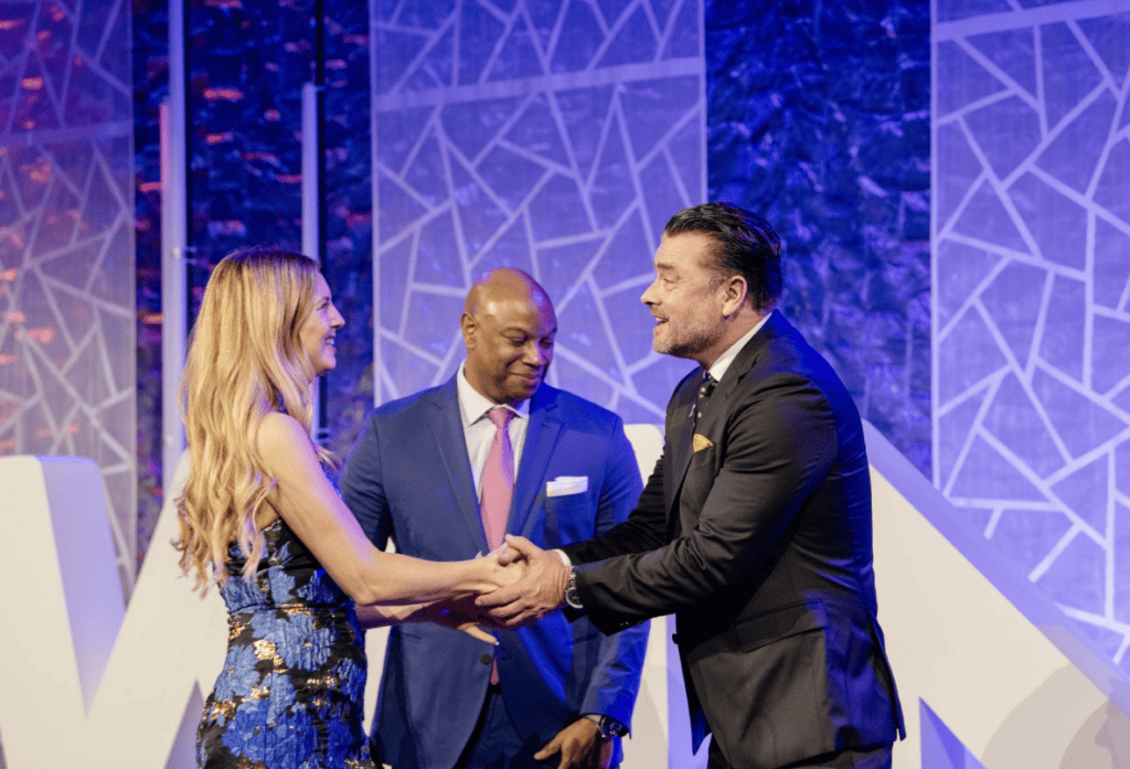 A man and woman embrace hands on stage as another man looks on