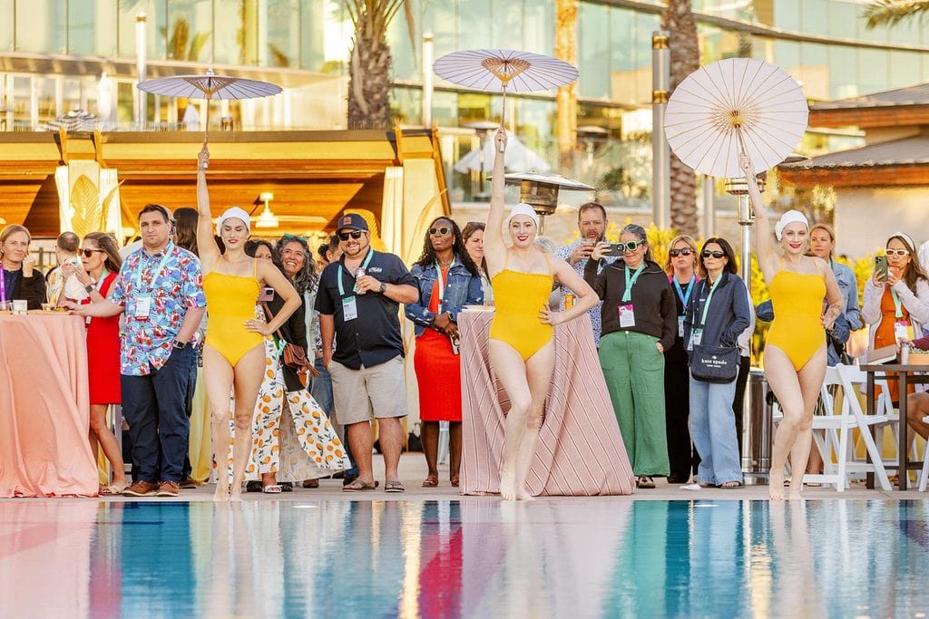 Group of models in yellow swimsuits posing by pool at resort event.