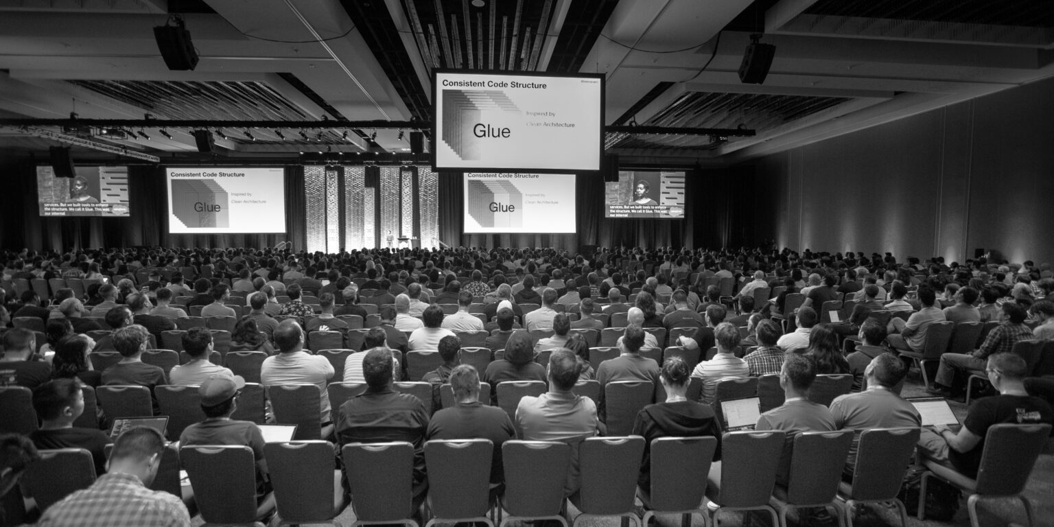 Group of people at a conference session with a video screen.