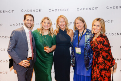 Five people in black tie attire posing in front of the photo wall during an event