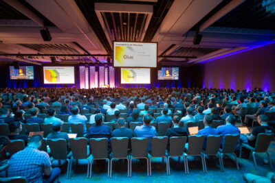 A larger group of people seated in a dark conference room with a video screen.