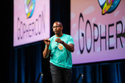 Man in a bright green T-shirt speaking on stage at a conference