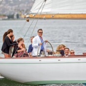 A group of people on a sailboat, with a man at the helm