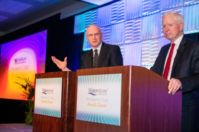 Two men speaking at a podium during a corporate event