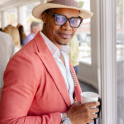 A man with a top hat and salmon colored suit poses with his coffee during a business conference