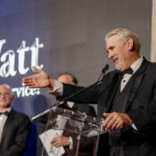 A man in a suit with a bowtie presenting at a podium during a business conference