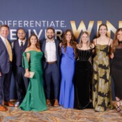 A group of people in formal evening attire pose at a business event in front of a backdrop that says "win"