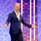 Main in a suit in front of a purple lit background smiles during a presentation on stage.
