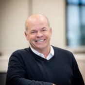 A man smiling with his arm on top of a cubicle wall