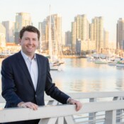 Man in suit posing on a dock with downtown San Diego in the background