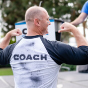 A man points to the "coach" lettering on the back of his shirt