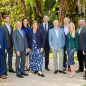 A group of business executives in formal attire pose outdoors in front of trees
