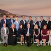 Group of people in business attire on the grass at sunset with the ocean in the background.