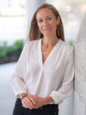 Headshot of a woman in a white top leaning against the side of a building