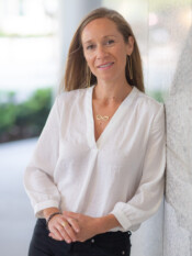 Headshot of a woman in a white top leaning against the side of a building