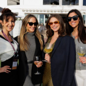 Four women pose with wine glasses during and outdoor business party