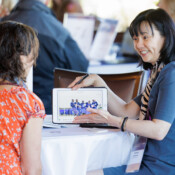 A woman showing images on a tablet to another woman during a business event